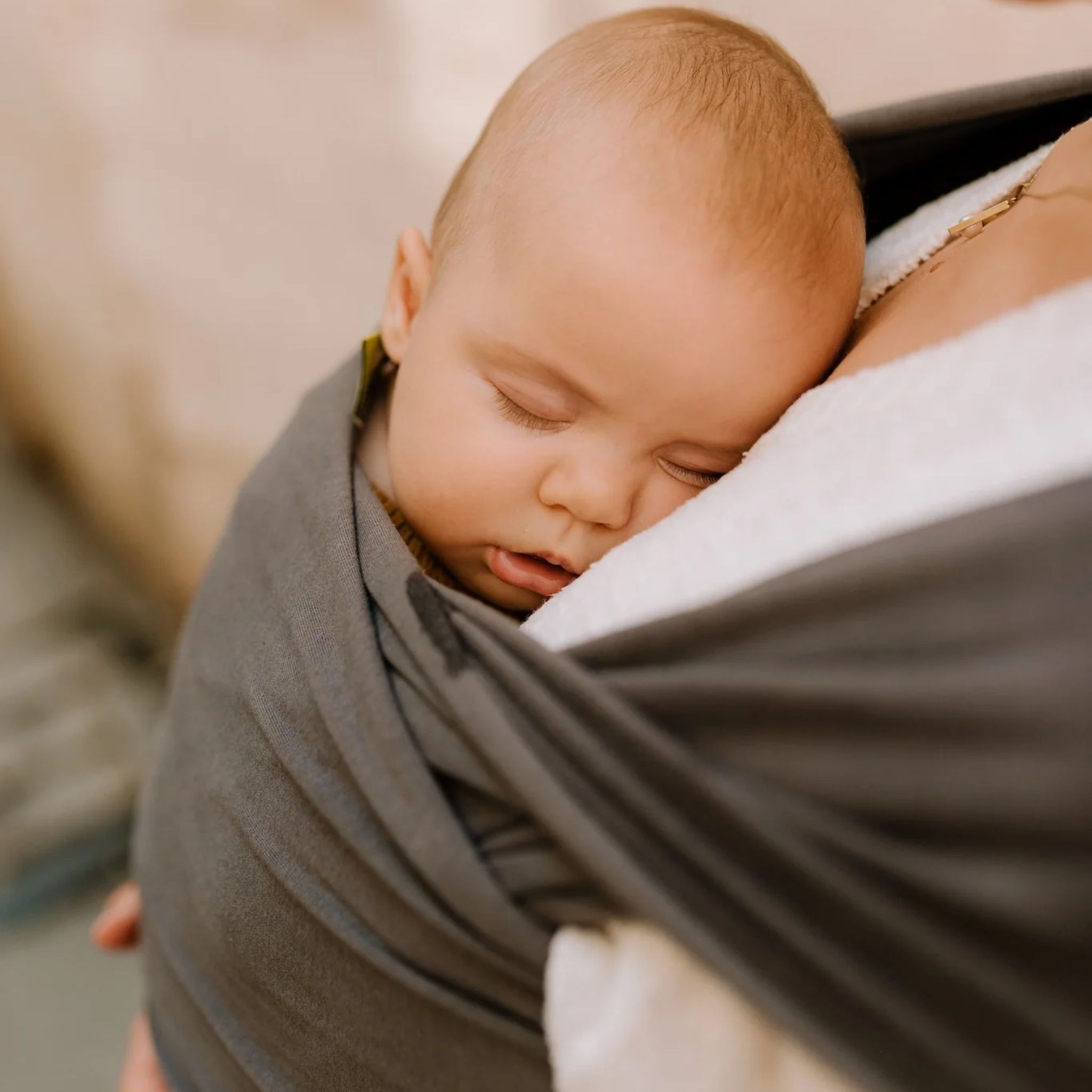Parent carrying newborn in organic dark grey wrap carrier outdoors
