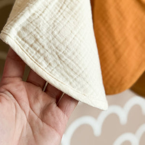 Close-up of a hand holding a white muslin burp coth against a blurred background