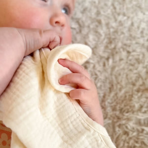 Baby holding a white burp cloth against a neutral background