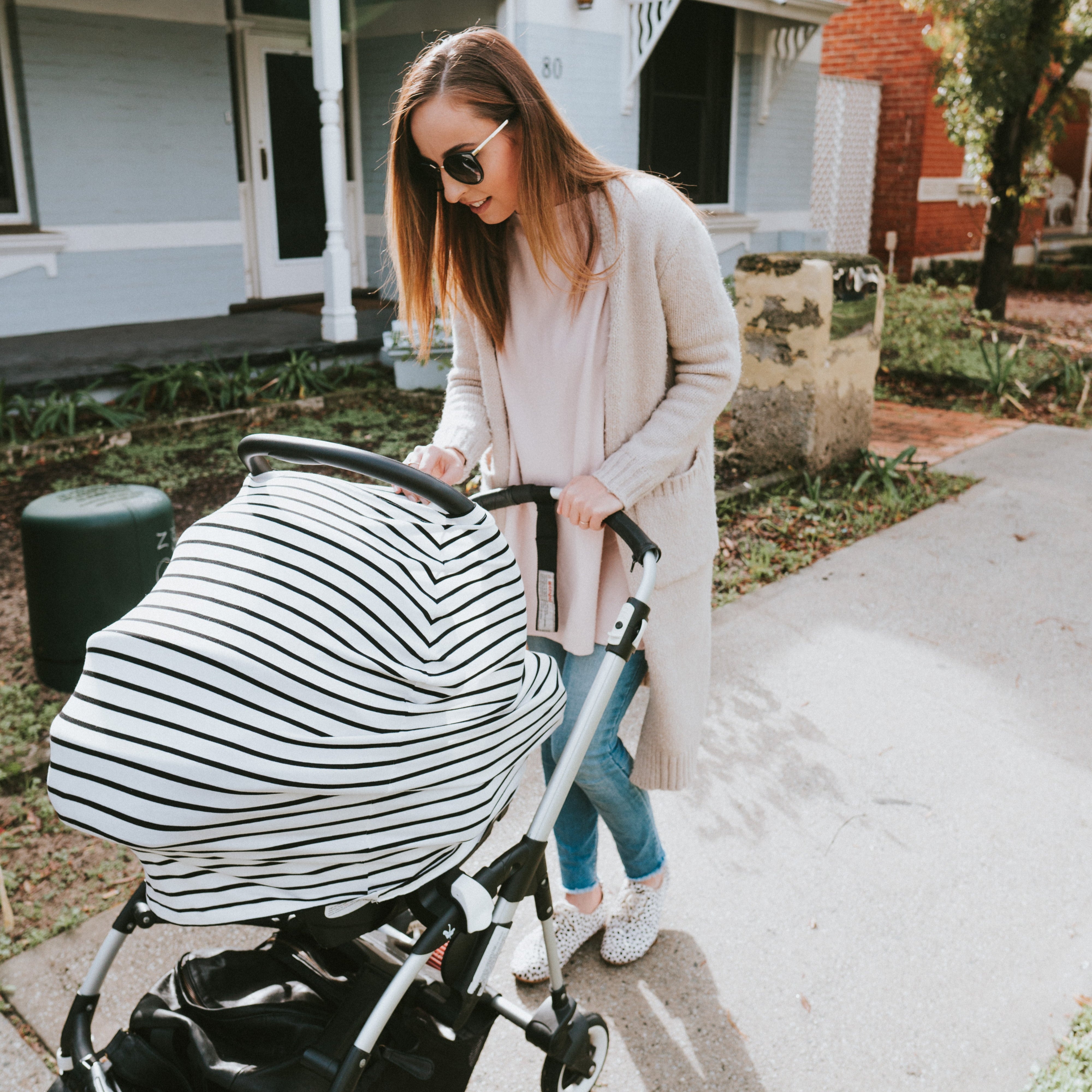 Woman pushing a stroller with a striped cover in front of a house.