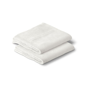 A folded white cotton knitted baby blanket on a plain background.
