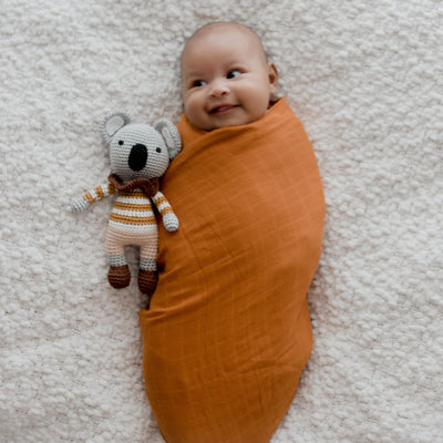 Three folded organic cotton muslin swaddles in warm savannah rust tone